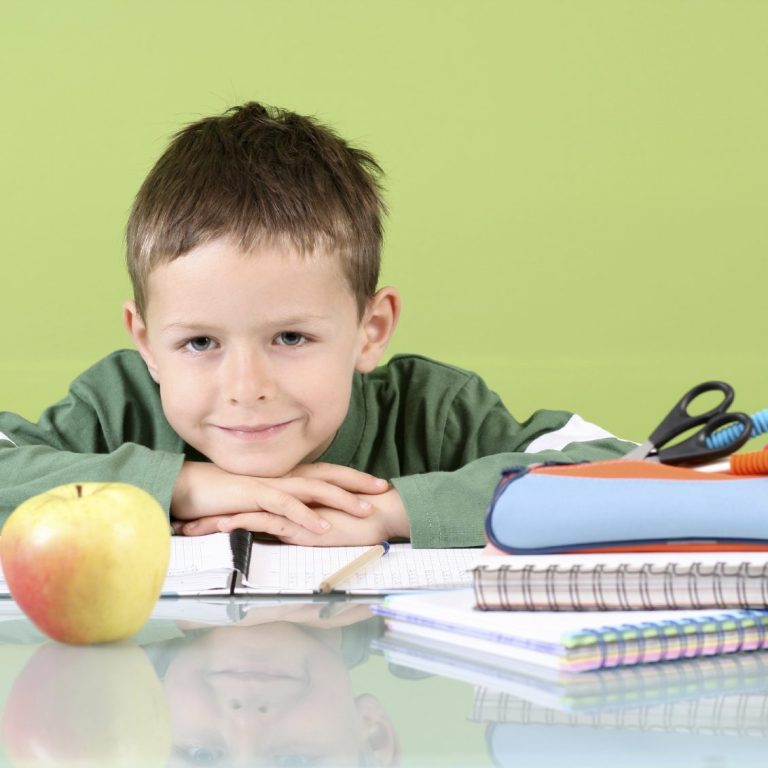 Ein Junge sitzt lächelnd am Tisch, vor ihm liegen Schulsachen aus seinem Nachhilfeunterricht.