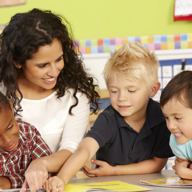 Eine Nachhilfe-Lehrerin lächelt zwei Schüler an. Die Schüler lächeln ebenfalls und lösen gemeinsam eine Aufgabe.