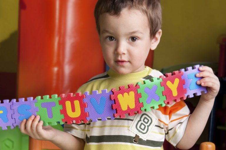 Ein kleiner Junge im Kindergarten hält stolz eine Kette mit dem ABC in die Kamera.